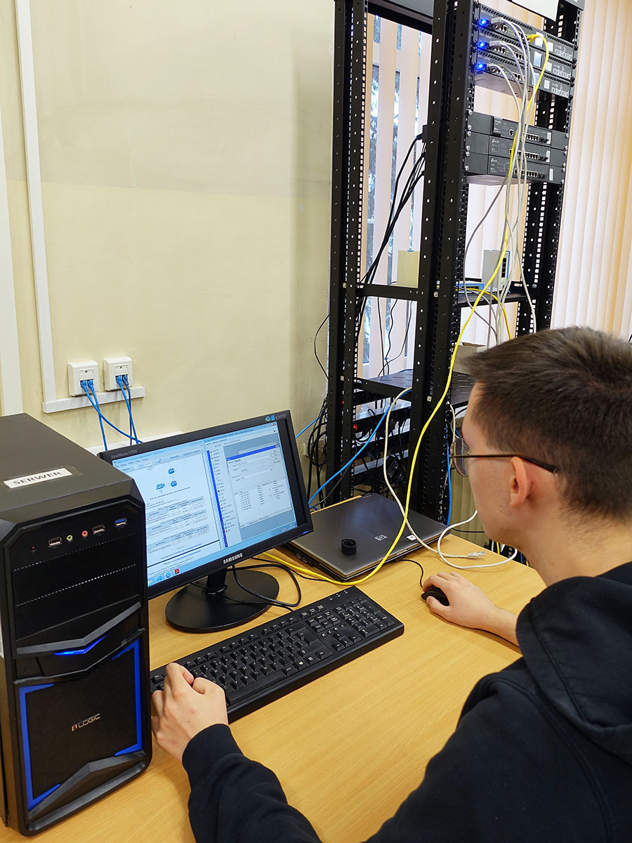 Uczeń technika teleinformatyka podczas zajęć z szafą teleinformatyczną w tle