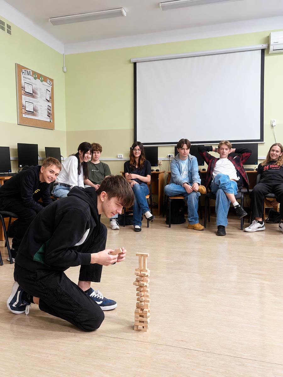 Uczeń buduje wieżę z drewnianych elementów, a pozostali uczestnicy obserwują ćwiczenie integracyjne