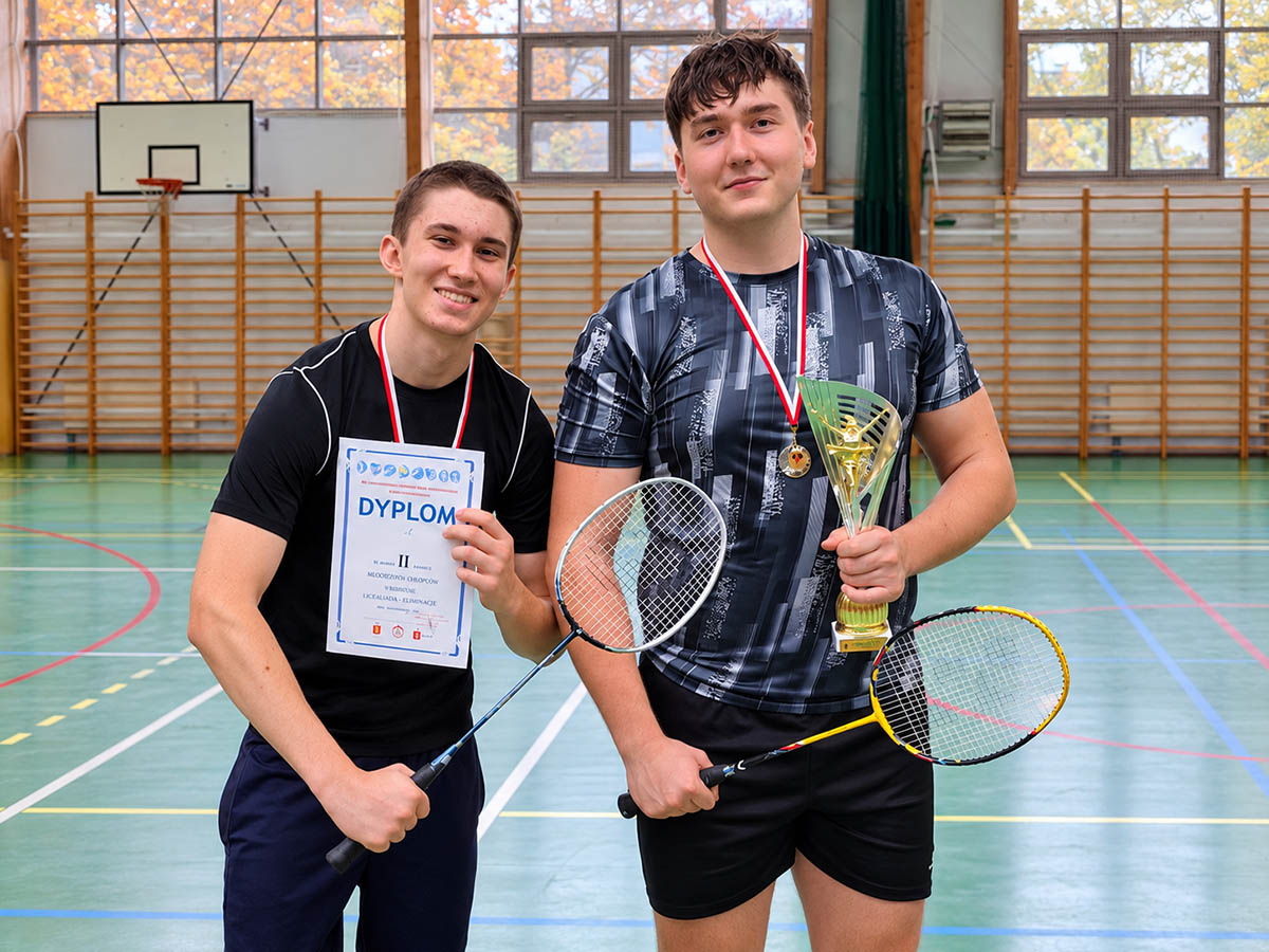 Dwóch zawodników z rakietami i dyplomem po mistrzostwach dzielnicy Praga-Południe w badmintonie