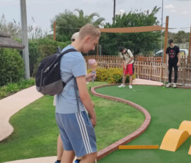 Uczeń wykonuje uderzenie kijem na torze do minigolfa.