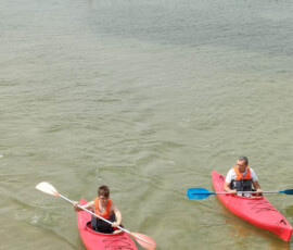 Uczniowie płyną kajakami w niewielkiej odległości od plaży.