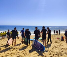 Uczestnicy zajęć surfingowych stoją na plaży blisko oceanu.
