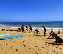 Uczestnicy wykonują ćwiczenia przygotowujące do surfingu na plaży.