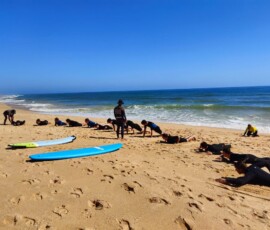 Uczniowie stoją przy deskach surfingowych podczas instruktażu na plaży.