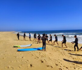 Grupa uczniów idzie po plaży z deskami surfingowymi.