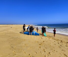 Uczniowie niosą deski surfingowe w stronę oceanu na Praia de Faro.