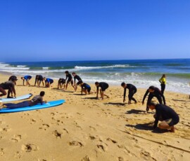 Grupa uczniów wykonuje dynamiczne ćwiczenia na plaży.