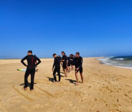 Uczestnicy stoją na plaży przy deskach, przygotowując się do surfingu.
