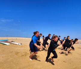 Uczniowie biegną po plaży w ramach rozgrzewki przed surfingiem.