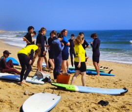 Uczniowie stoją przy kolorowych deskach surfingowych na plaży.