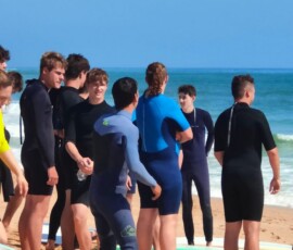 Kilku uczniów słucha instruktażu przy deskach surfingowych.