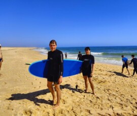 Uczniowie przygotowują niebieską deskę surfingową na plaży.