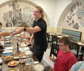 Uczniowie siedzą przy stole z portugalskimi potrawami podczas pożegnalnego spotkania.