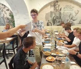 Uczniowie stoją i rozmawiają przy stole podczas podsumowania praktyk w Faro.