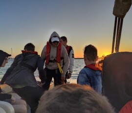 Uczeń siedzi na pokładzie łodzi podczas spokojnego rejsu o zachodzie słońca.