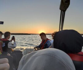 Uczniowie siedzą na łodzi i obserwują morze podczas wieczornego rejsu.
