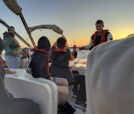 Pomarańczowe słońce zachodzi nad wodą podczas rejsu Erasmus+ w Faro.