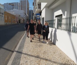 Grupa uczestników Erasmus+ spaceruje chodnikiem przy białych budynkach.