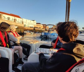 Grupa uczniów w kamizelkach ratunkowych siedzi na pokładzie podczas rejsu Erasmus+.