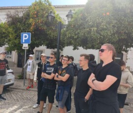 Uczniowie stoją przy zabytkowych murach i słuchają przewodnika w Faro.