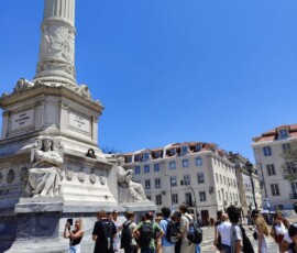 Wysoki pomnik na lizbońskim placu z grupą uczniów u podstawy.