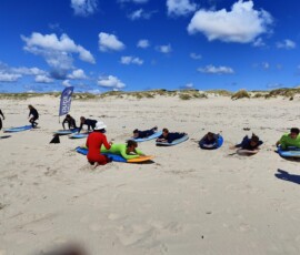 Uczestnicy Erasmus+ ćwiczą podstawy surfingu na piaszczystej plaży.