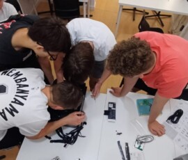 Uczniowie wspólnie wykonują zadanie techniczne przy stole w miejscu praktyk.