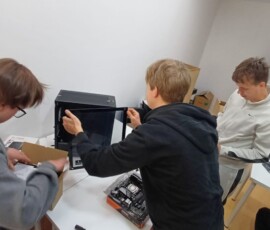 Grupa uczniów montuje i sprawdza elementy komputera podczas praktyk zawodowych.