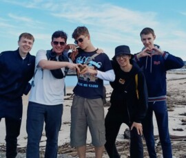 Grupa uczniów pozuje na skalistym wybrzeżu z oceanem w tle.