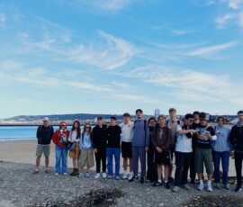 Grupa uczniów i opiekunów pozuje na plaży podczas majowej wycieczki.