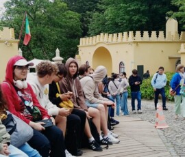 Grupa uczniów siedzi w ogrodzie podczas całodniowej wycieczki.