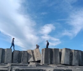Uczestnicy stoją na dużych betonowych konstrukcjach przy wybrzeżu.