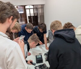 Uczniowie skupieni wokół otwartego komputera wspólnie wykonują zadanie techniczne.