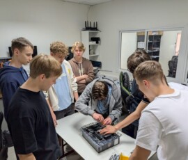 Uczniowie stoją wokół stanowiska i wspólnie pracują nad komputerem.