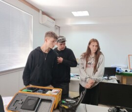 Uczniowie oglądają urządzenia i narzędzia na stole podczas praktyk zawodowych.
