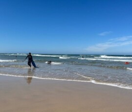 Grupa uczestników Erasmus+ wychodzi z oceanu po ćwiczeniach surfingowych.