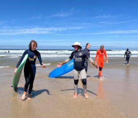 Uczniowie wracają z deskami na plażę po lekcji surfingu.