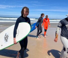 Uczestnicy Erasmus+ idą z deskami surfingowymi po plaży podczas zajęć nad Atlantykiem.
