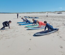 Uczestnicy Erasmus+ ćwiczą z deskami surfingowymi na piasku.