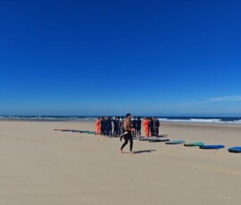 Uczniowie ćwiczą pozycję na desce surfingowej na plaży.