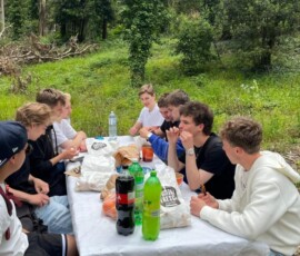 Uczniowie odpoczywają przy czerwonym stole podczas pikniku.