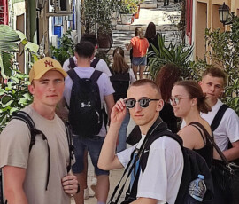 Uczniowie i opiekunowie stoją na kolorowej uliczce podczas zwiedzania Alicante.