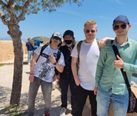 Uczniowie i opiekunowie stoją w cieniu drzewa na terenie zwiedzanego wzgórza w Alicante.