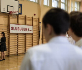 Uczniowie w białych koszulach podczas uroczystości ślubowania klas pierwszych ZSŁ w sali gimnastycznej