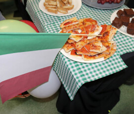 Pizza, słodkie przekąski i dekoracja w barwach włoskiej flagi na szkolnym stoisku.