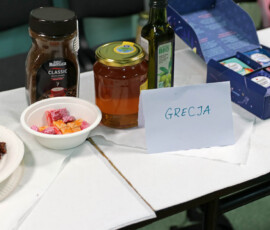 Słoiki i przekąski na stole oznaczonym napisem „Grecja” podczas Dnia Języków 2026.