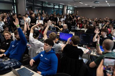 Uczestnicy pracują przy stołach w dużej sali podczas hackathonu HackCarpathia 2026.